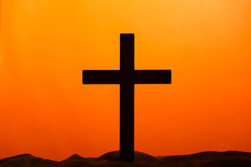 Wooden cross on sand against orange background. Good Friday concept