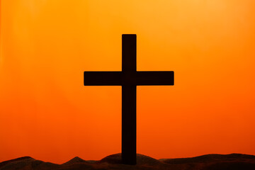 Wooden cross on sand against orange background. Good Friday concept