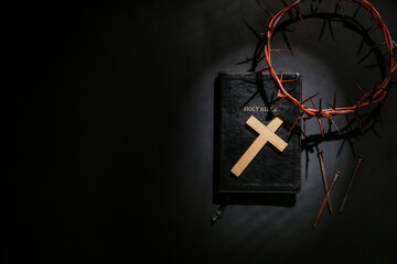 Wooden cross with crown of thorns, Bible and nails on black background. Good Friday concept
