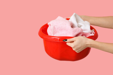 Woman holding basket with clean laundry on pink background