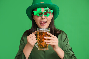 Beautiful young woman in leprechaun hat and decorative glasses in shape of clover with glass of...