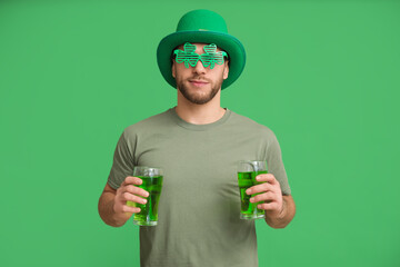 Young man in leprechaun hat with glasses of beer on green background. St. Patrick's Day celebration