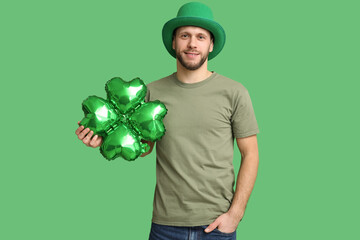 Young man in leprechaun hat with air balloon in shape of clover on green background. St. Patrick's...