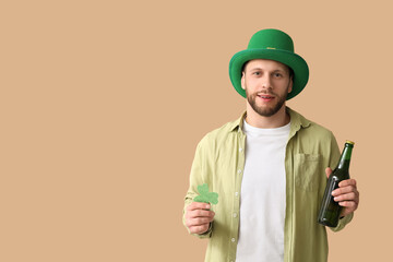 Young man in leprechaun hat with bottle of beer and clover on brown background. St. Patrick's Day...
