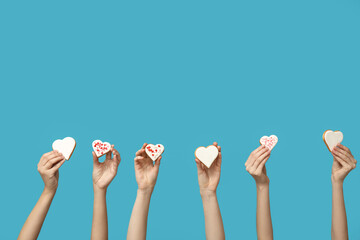 Women with heart-shaped cookies on blue background. Valentine's Day celebration - obrazy, fototapety, plakaty
