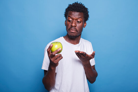 Young black man showcasing green apple to camera in studio. Portrait shot of african american individual holding fruit with natural vitamins for organic lifestyle and healthy nutrition.