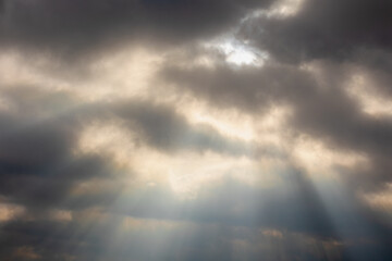 Fototapeta na wymiar Ray of sun or sunbeam shining through the cloudy cumulus clouds floating in the skies, White grey fluffy clouds on sky before raining, Nature pattern background.