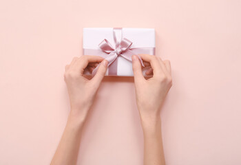 Female hands with gift box on pink background. International Women's Day