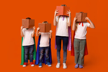 Cute kids dressed as superhero covering faces books on orange background. Library Lovers Day