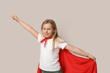 Cute teenage girl dressed as superhero on grey background