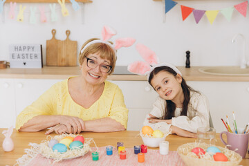 Obraz na płótnie Canvas Happy grandmother and granddaughter in easter bunny ears having egg tapping with easter eggs