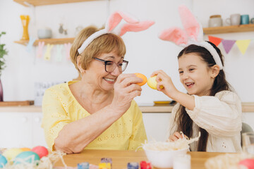 Obraz na płótnie Canvas Happy grandmother and granddaughter in easter bunny ears having egg tapping with easter eggs