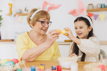 Happy grandmother and granddaughter in easter bunny ears having egg tapping with easter eggs