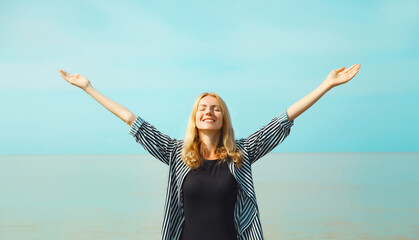 Summer vacation, happy young woman raising her hands up on the beach on sea