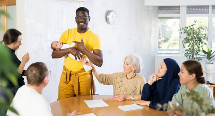 Positive caring african american man holding baby in arms, playing with child of female coworker...