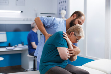 Fototapeta premium Osteopathic doctor cracking back and shoulder bones for retired old woman at chiropractic consultation. Chiropractor giving assistance to elderly patient for recovery and rehabilitation.