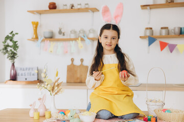 A beautiful child girl sitting on the table with decoratioons and painting colorful eggs