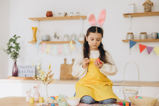 A beautiful child girl sitting on the table with decoratioons and painting colorful eggs