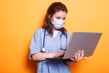 Healthcare specialist wearing face mask looking at laptop and wearing uniform and stethoscope....