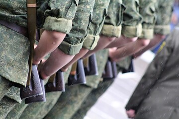 the hands of soldiers and their weapons in green uniforms in formation