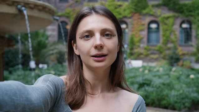 young  influencer social media streaming video in park speaking on camera while video calling or going live. Cute female recording promo vlog Selfie video in picturesque place. ugc. 