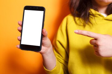 Photo focus on caucasian hand vertically grasping mobile device showing isolated mockup template in studio. Close-up of female individual holding and pointing to cell phone with white screen display.