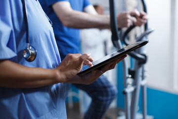 Doctor in blue scrubs and a stethoscope is closely examining a healthcare report on digital device...