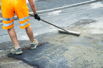 Operator washing asphalt on street with broom with boots and florescent uniform