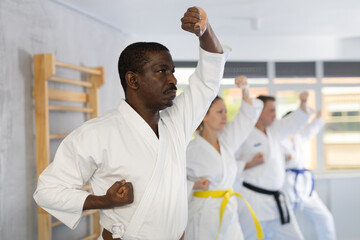 Diligent middle-aged male attendee of karate classes practicing kata standing in row with others in sports hall