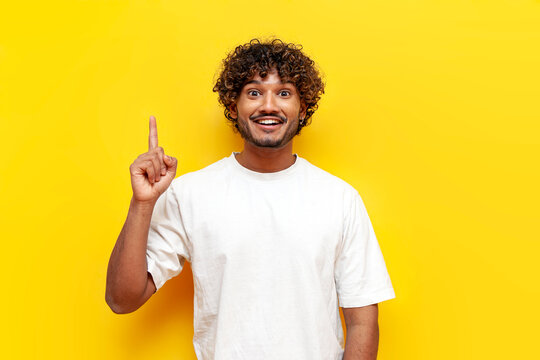 I have an idea. young indian man in white t-shirt raises his finger and points up on yellow isolated background, curly guy knows solution and idea