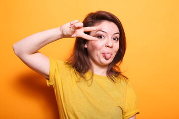 Portrait of caucasian female individual doing peace sign and having her tongue out, showing victory...