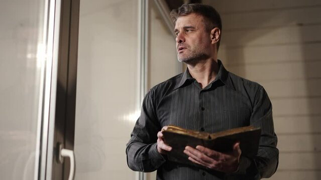 Man at home, prayer reading old literature. Man in black shirt holding religious holy book. Hope for salvation. Exploration of traditional spiritual scripture. Searching for god