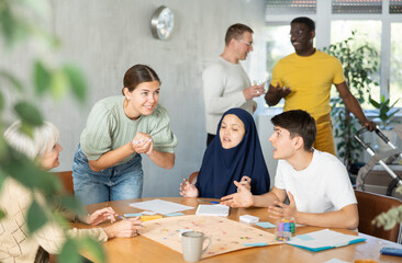 Group of multinational men and women playing game while sitting at table in office
