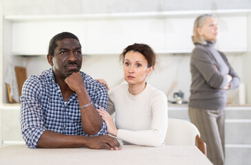 Fototapeta premium Wife calms husband down during family quarrel with mother-in-law