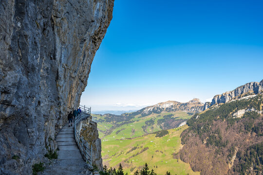 Tourists walk on alpine trail from &Auml;scher to Ebenalp under a big rock wall with Hoher kasten mountin in the background. Seealpsee, Appenzell, Switzerland, Europe.