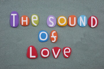 The sound of love, creative slogan composed with hand painted multi colored stone letters over green sand