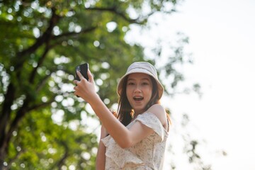 Beautiful young asian woman wearing a hat using phone in a nature park