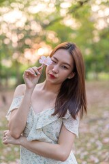 Beautiful young asian woman enjoying nature during sunset moments at a public park with lots of sakura flowers