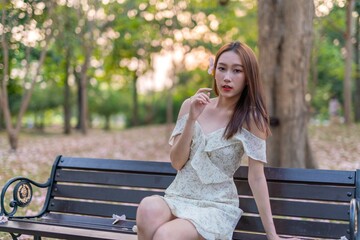 Naklejka premium Beautiful young asian woman enjoying outdoor breeze during sunset moments at a public park with lots of sakura flowers