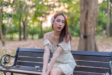 Naklejka premium Beautiful young asian woman enjoying outdoor breeze during sunset moments at a public park with lots of sakura flowers