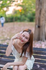 Beautiful young asian woman enjoying outdoor breeze during sunset moments at a public park with lots of sakura flowers