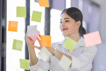 Business Asian woman meeting at office and use post it notes in glass wall to share idea....