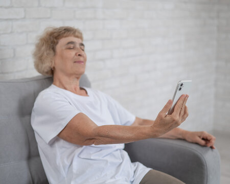 An elderly Caucasian woman suffers from farsightedness and tries to read a message on a smartphone with her arm outstretched. 