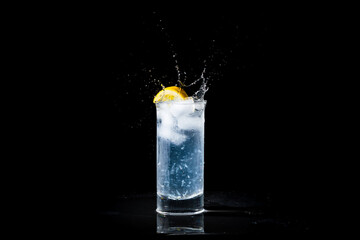 Glass of water and lemon splashing in summer drink. Refreshing drink with splash droplets isolated on black background with copy space