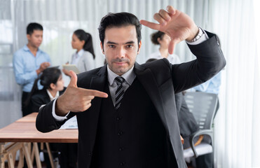 Portrait of happy businessman looking at camera, making hand holding gesture for advertising product with motion blur background of business people movement in dynamic business meeting. Habiliment