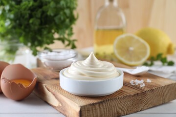 Fresh mayonnaise sauce in bowl and ingredients on white wooden table