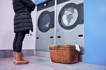 Unrecognizable woman standing in front of industrial dryer waiting with an empty basket to dry her...