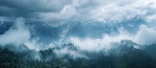 Fototapeta premium From above, the contrasting beauty of nature is seen: clouds veiling majestic peaks, the sky peeking through, and a mix of forest and clear-cuts in the foreground while gray clouds approach.