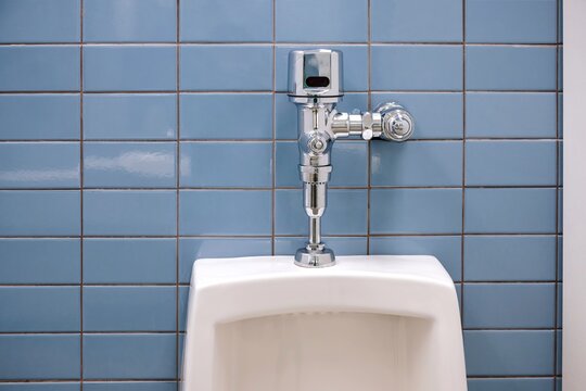 Close up of an auto flushing ceramic urinal toilet with chrome motion sensor detector. Water conservation, green energy, environment protection background. 