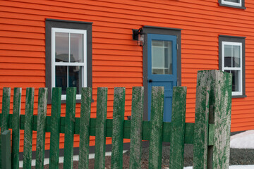 The exterior facade of a bright orange vintage building with green trim, blue door, wood clapboard...